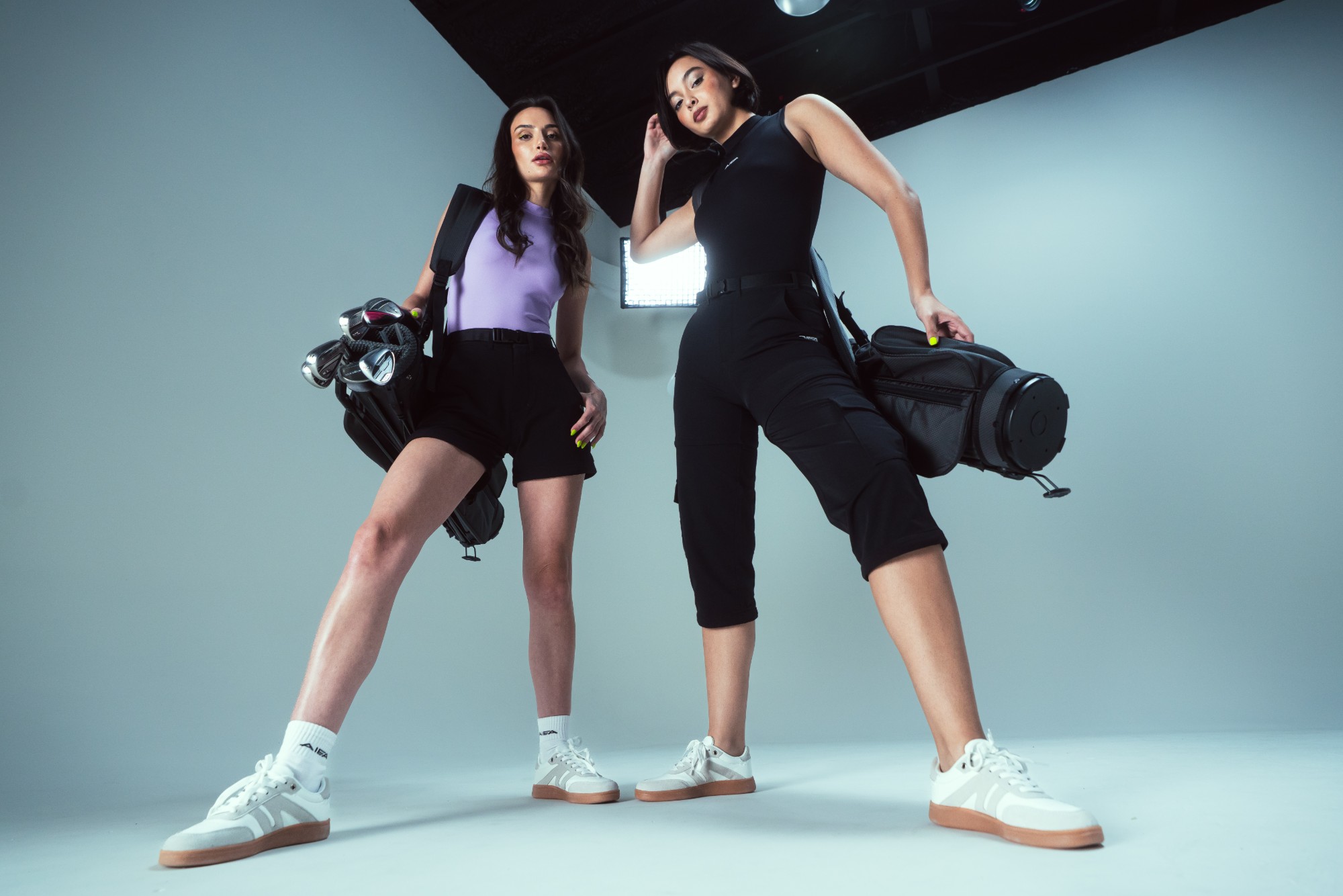 Two models in Collection 02 carrying golf bags and irons, shot from a low angle