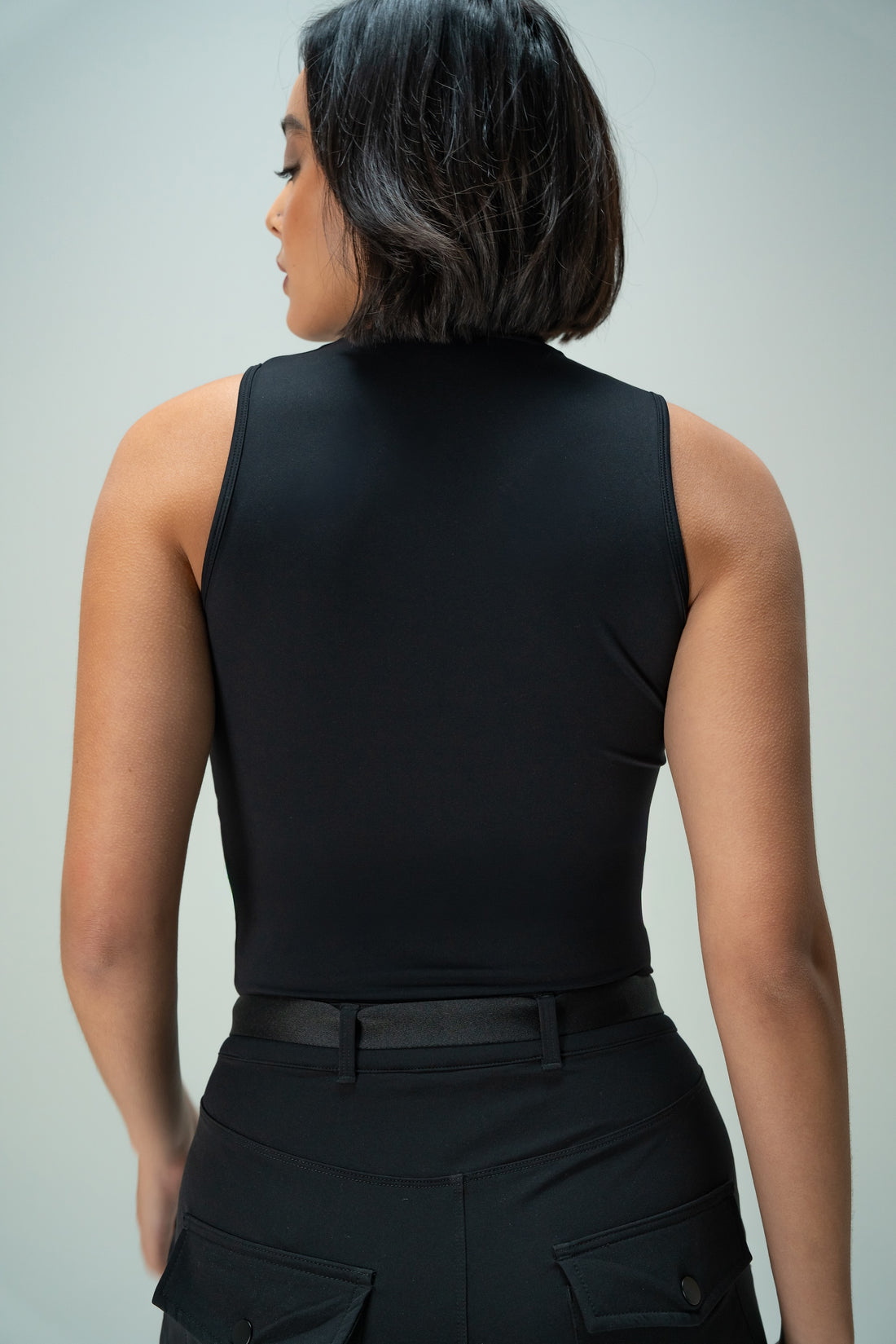 Person wearing a black sleeveless top and black pants against a gray background